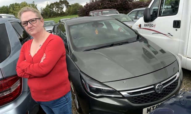 Michelle Clarke pictured in a red jumper and blue jeans beside her grey Vauxhall Astra.