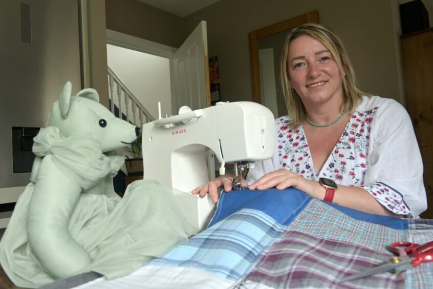 Andrea sitting at her sewing machine with her white bear with a patch work quilt.