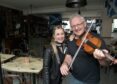 A blonde woman and a grey-haired man holding a fiddle looking at the camera standing side-by-side in a pub.