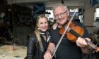 A blonde woman and a grey-haired man holding a fiddle looking at the camera standing side-by-side in a pub.