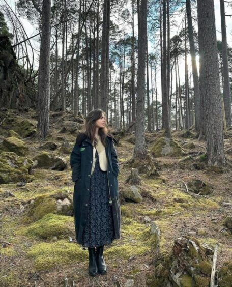 Lily Collins pictured in a long coat in a pine forest in the Highlands.