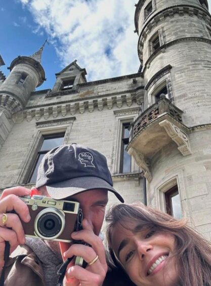 Lily Collins and her husband Charlie McDowall pictured taking a selfie outside Dunrobin Castle as Charlie holds a camera up to his eye.