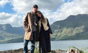 Lily Collins posing with her husband Charlie McDowell in front of a river and hill in the Highlands.