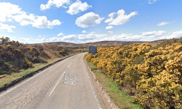 A836 east of Melvich with clear blue skies overhead, bushes on both sides and hills up ahead.