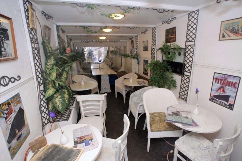 A view of the Cafe Parisien, with white tables and chairs, plants and posters put together by Stan inside his Titanic replia. 