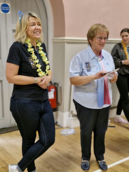 Nicola Youngson wearing a yellow garland as she receives an award from Shirley Milton the Girlguiding county president, wearing a light blue blouse.