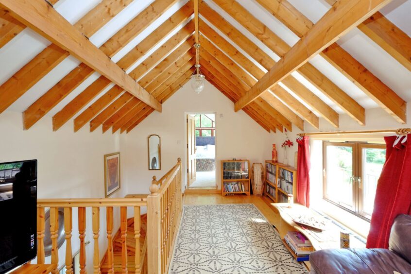 A potential work space in the home with slated ceilings with wooden support beams. There are small bookcases in the corner next to a window