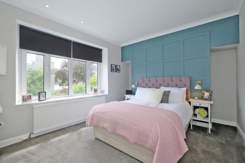 One of the bedrooms with a dusty blue accent wall and pink bedding on the double bed. The walls are white and the carpet is grey