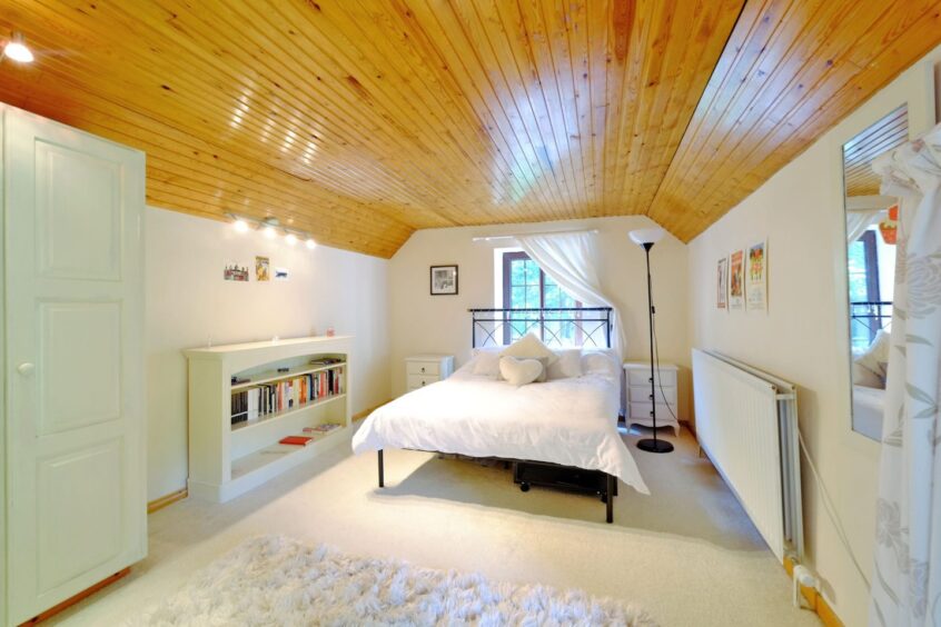 One of the bedrooms with cream furnishings and a pinstripe wooden ceiling 