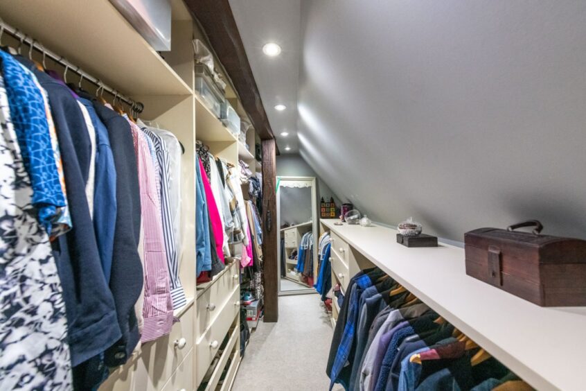 A walk-in wardrobe with rails of clothing and a full-body mirror at the end of the room