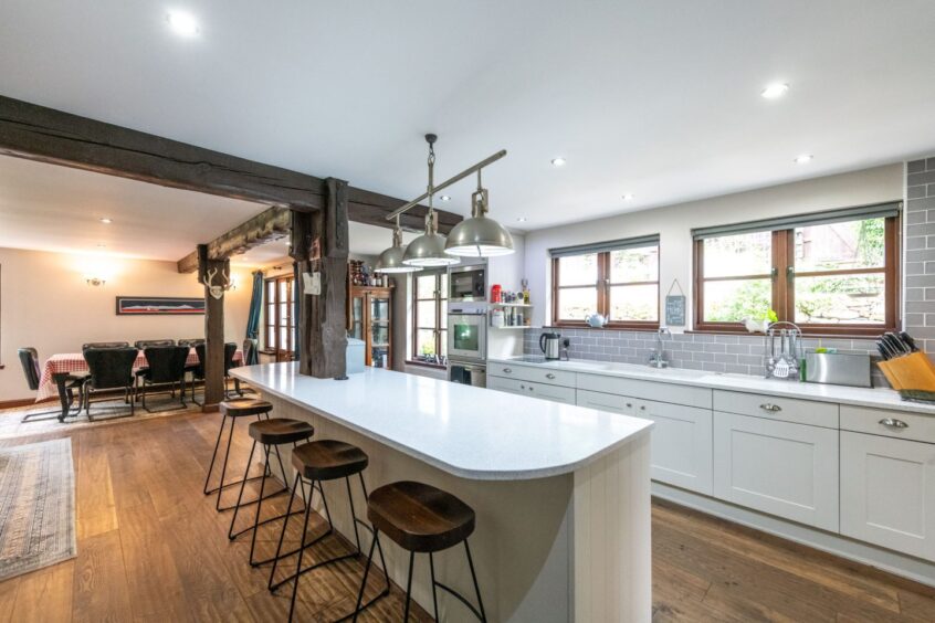 An open plan kitchen and dining area, with sleek white counters and dark wood tones