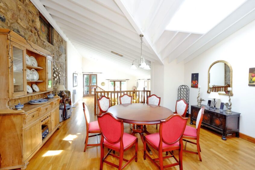 The dining area with a large round table and eight chairs. The walls are an airy white with an exposed stone accent wall.