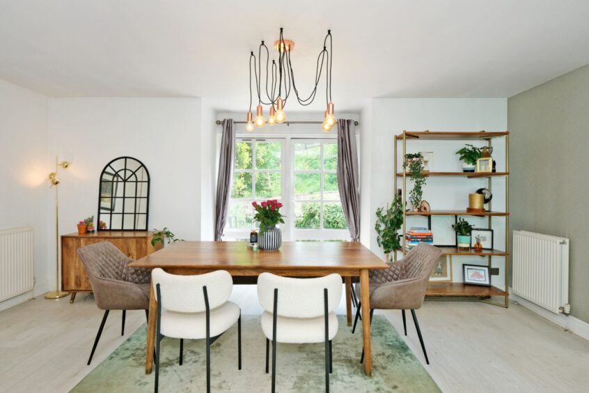 The dining area, with plush chairs and a wooden table, a statement light fixture and a lots of house plants