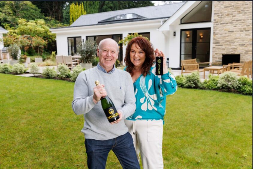 Rachael, wearing white trousers and green blouse, next to her husband Darren, wearing blue jeans and a grey jumper in the garden of their new £3 million Surrey home.