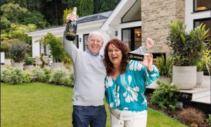 Rachael, wearing white trousers and green blouse, next to her husband Darren, wearing blue jeans and a grey jumper in the garden of their new £3 million Surrey home.
