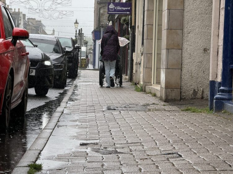 wheelchair user moving down rainy dingwall high street