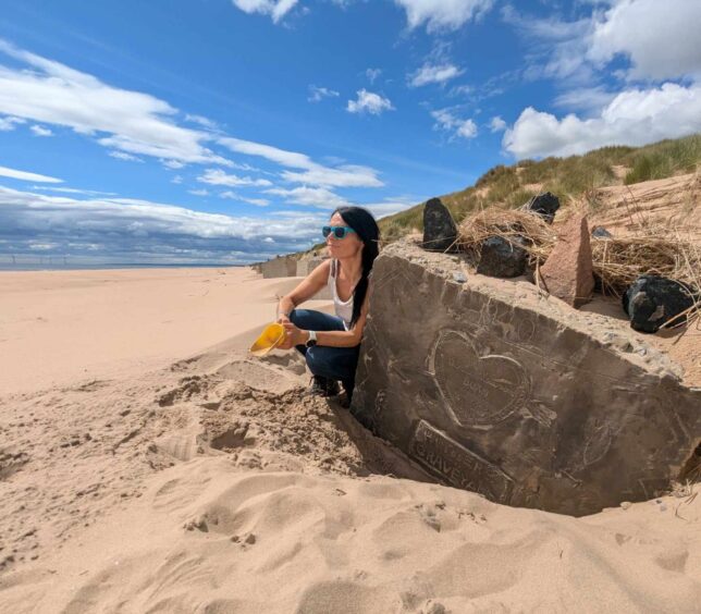 Gayle used her plastic scoop to expose the 'Hitler's Graveyard' artwork on the anti-tank block on Newburgh beach. Image: Gayle Ritchie.