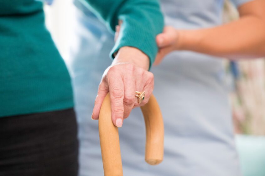 Carer helping woman with walking stick 