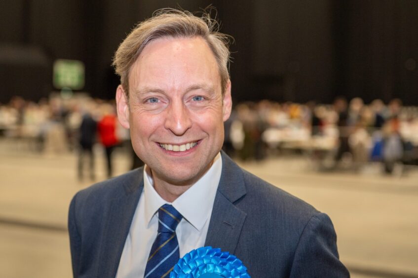 Liam Kerr wearing a suit and tie and a blue rosette in the election hall