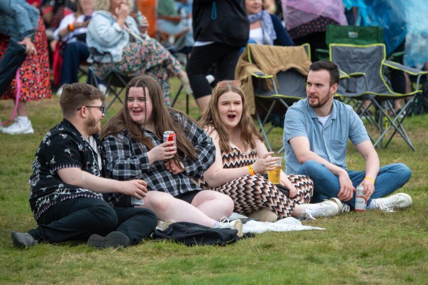 Four people sitting on grass with a drink