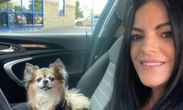 Michelle, pictures with dark hair and sunglasses on her head, next to her dog Benji in her taxi.