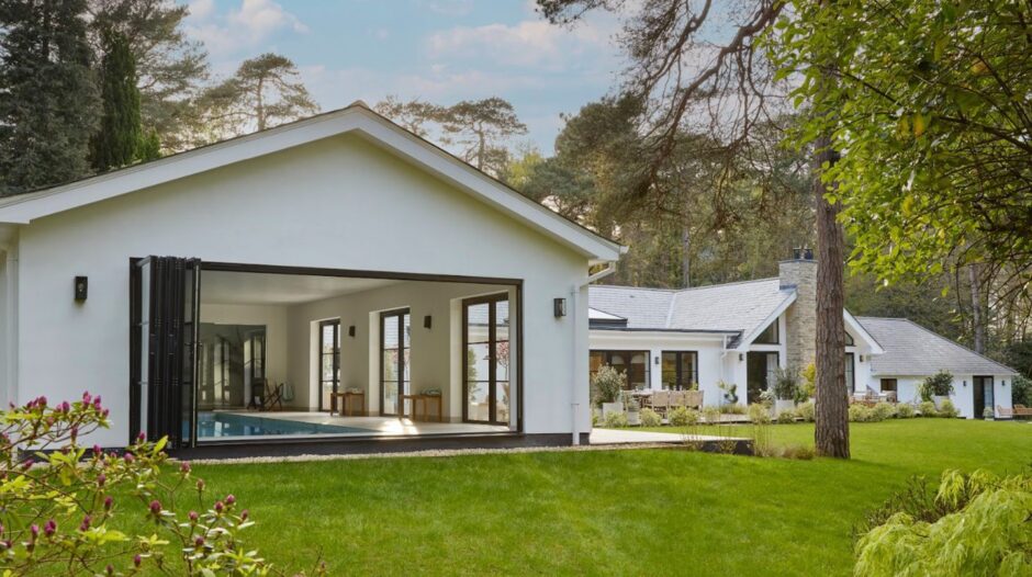 White luxury house surrounded by grass and forest.