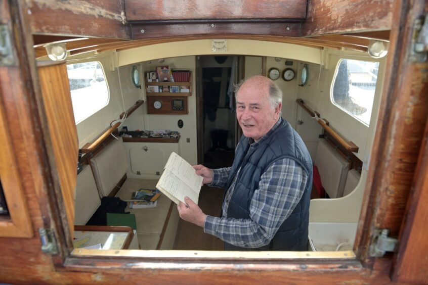 Eddie Rebbeck aboard his yacht with a log book of his journies to Scotland. 