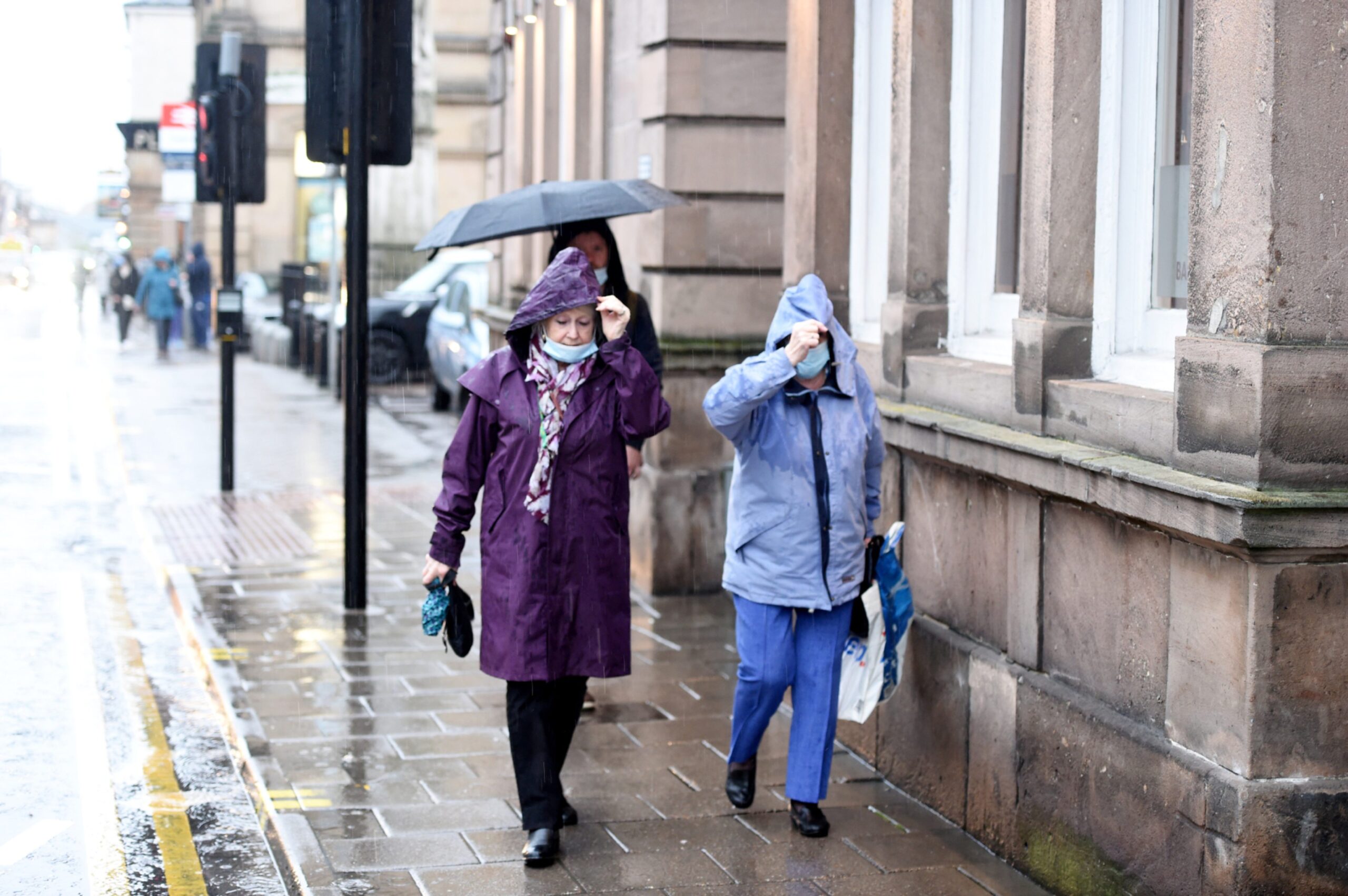 Two women walk down a street in Inverness in heavy rain.