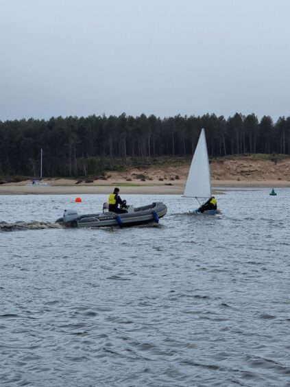 Person on a powerboat on blue water with a backdrop of a golden beach and trees in the distance. 