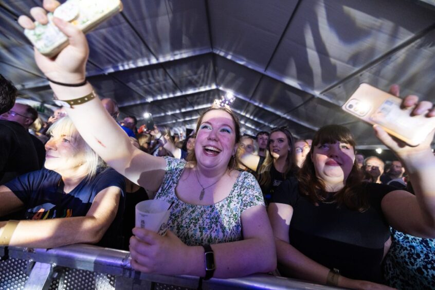 Female at the barrier in Speyfest holding up her phone.