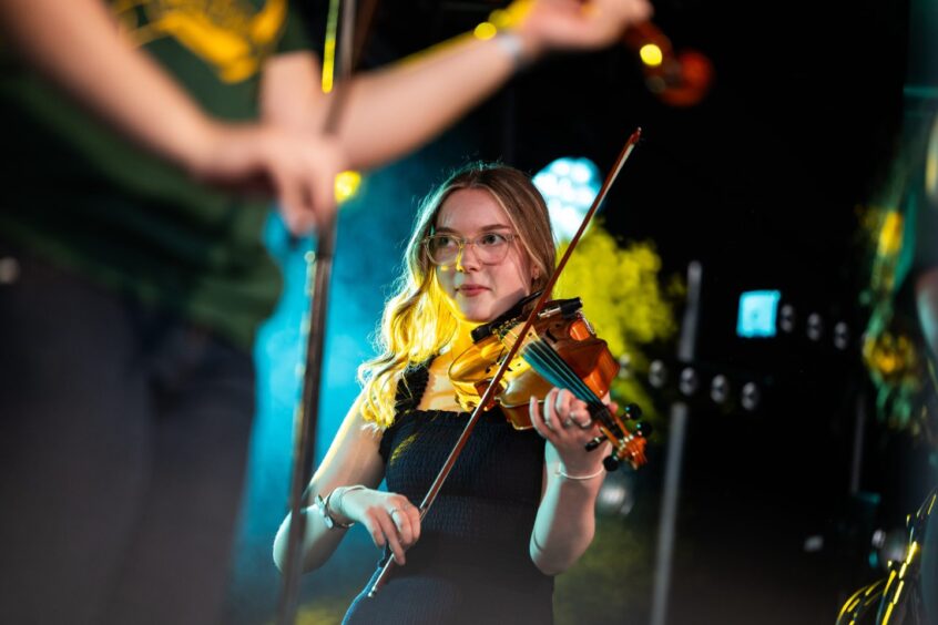 Female playing the violin in a black dress with turquoise background.