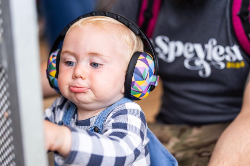 A young boy dressed in a checked shirt pouting his lip wearing a pair of ear defenders.