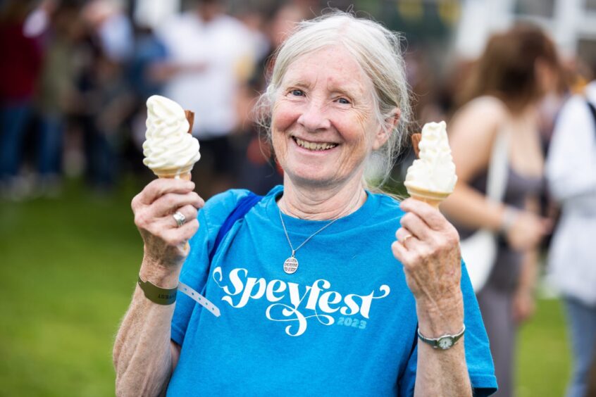 Woman wearing a blue t-shirt holds an ice cream cone in each hand.