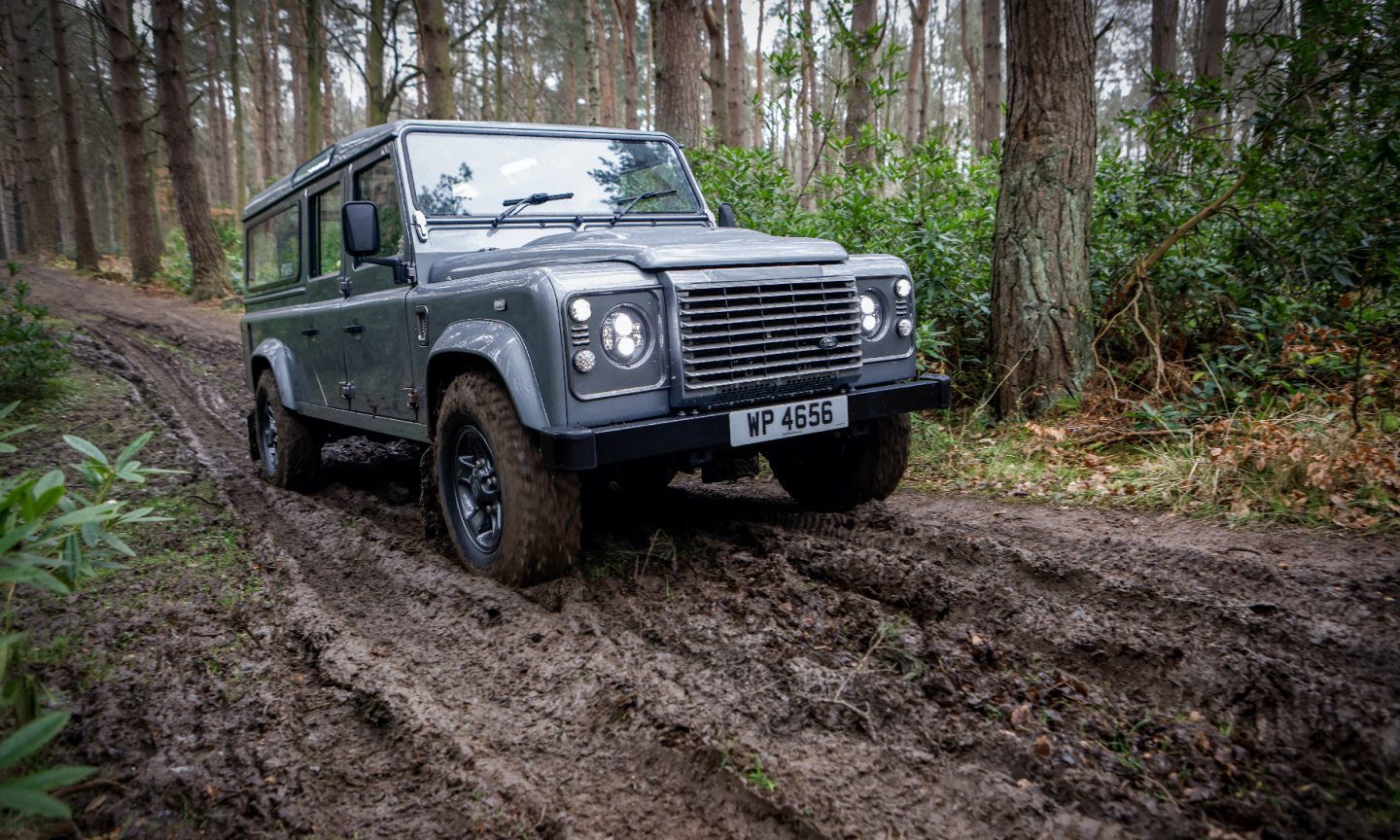 Silver and Rover Defender driving along muddy track in woodland.