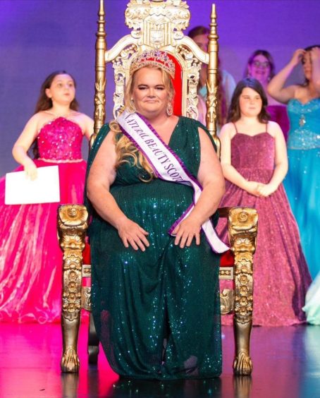 Clair Clark pictured in a green sparkly dress sitting on a throne wearing a crown.