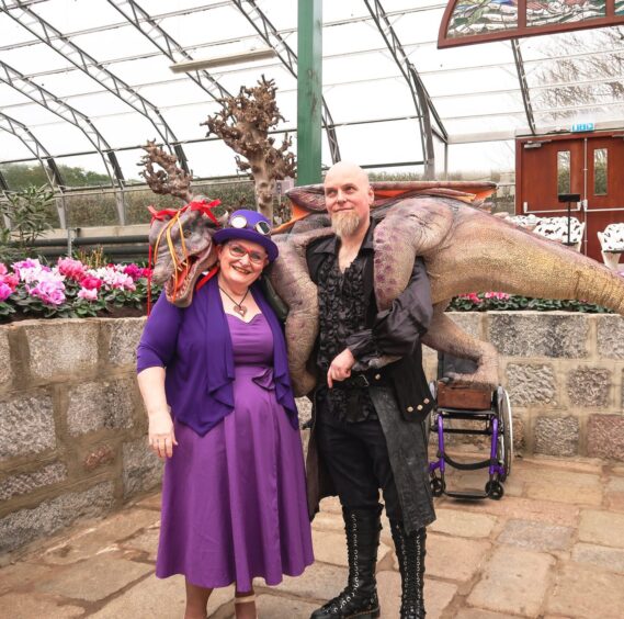 Isabel in a steampunk themed outfit in purple and man next to her with a dinosaur.