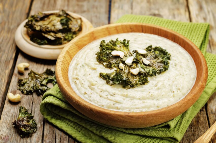 A delicious-looking cauliflower and kale soup in a wooden bowl