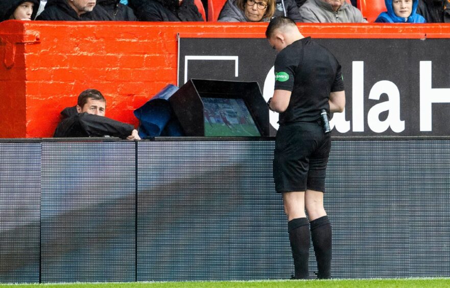 Referee Matthew MacDermid checks the VAR monitor for a potential red card for Brad Lyons during the William Hill Premiership match between Aberdeen and Kilmarnock at Pittodrie, on August 25, 2024. Image: SNS.