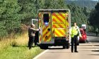 Ambulance parked on the carriageway with woodland around as a police officer directs traffic.