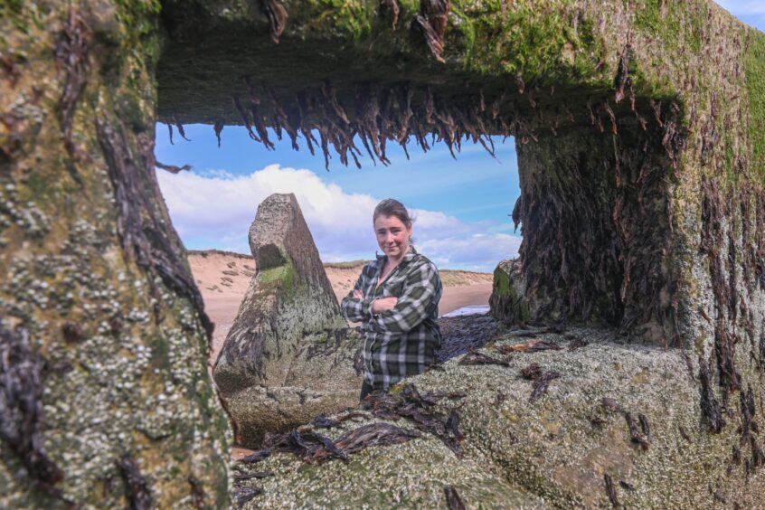 Jacqueline Willis looking at the camera through the window of a WWII pillbox on Donmouth Beach