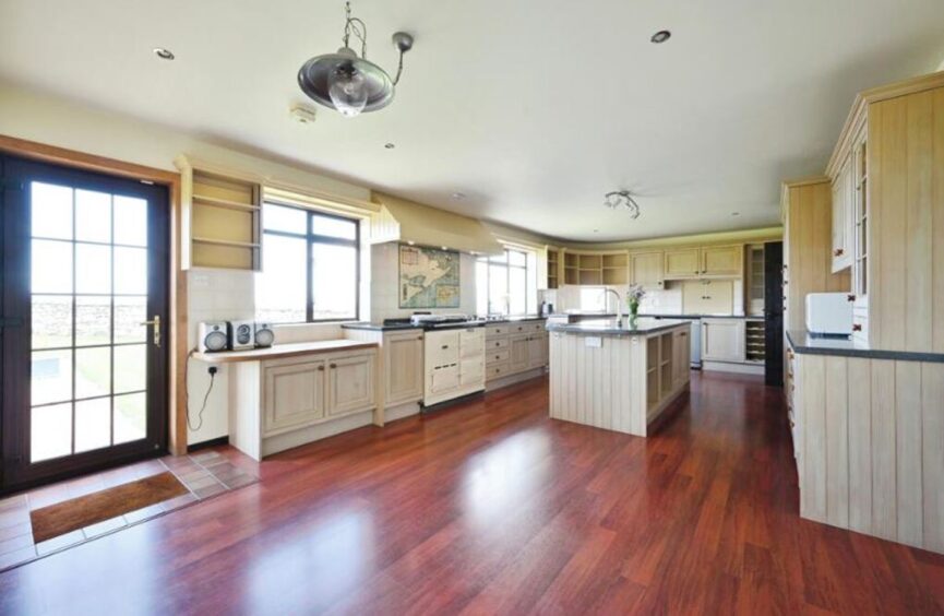 Large open kitchen at the Easter Ross B&B, featuring burgundy flooring and white cabinets. 