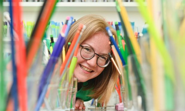 Sarah Holmes smiling at camera through tunnel of pencils.