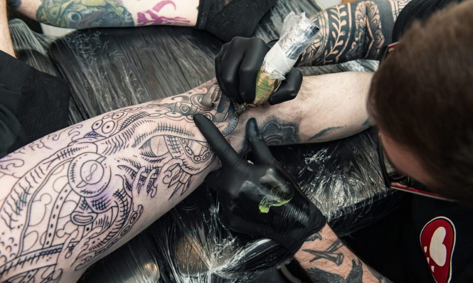 Looking down on Mike Farquhar tattooing a leg. 