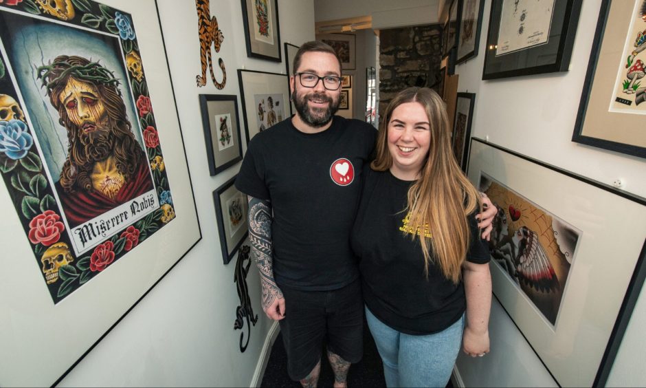 Mike Farquhar and Abbie Cummings inside South Street Electric Tattoo with artwork on walls. 