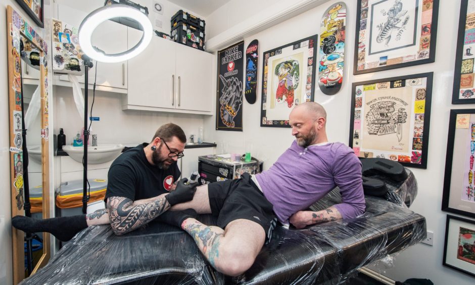 Mike Farquhar tattooing man's leg in tattoo studio 