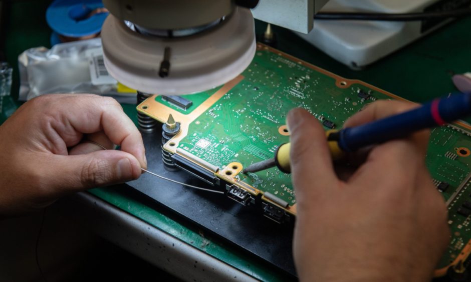 Close-up of hands working on circuit board. 