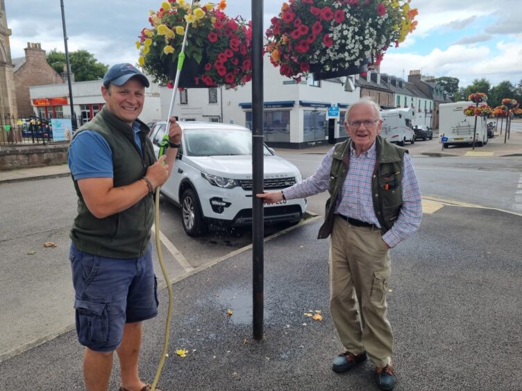 James standing below the hanging baskets in Beauly which he's been helping to tend for years. Pictured with Johnny Sugden of Campbell's of Beauly, James's former family business. 