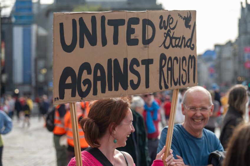 Woman holds 'United we stand against racism' sign at Aberdeen protest.