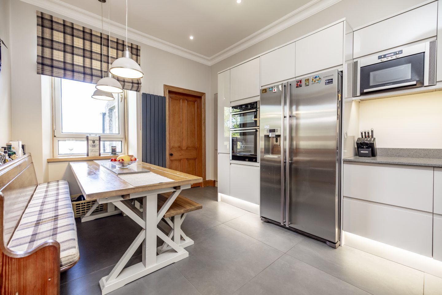 The kitchen has sleek white cupboards with grey countertops and a wooden dining table with bench seating