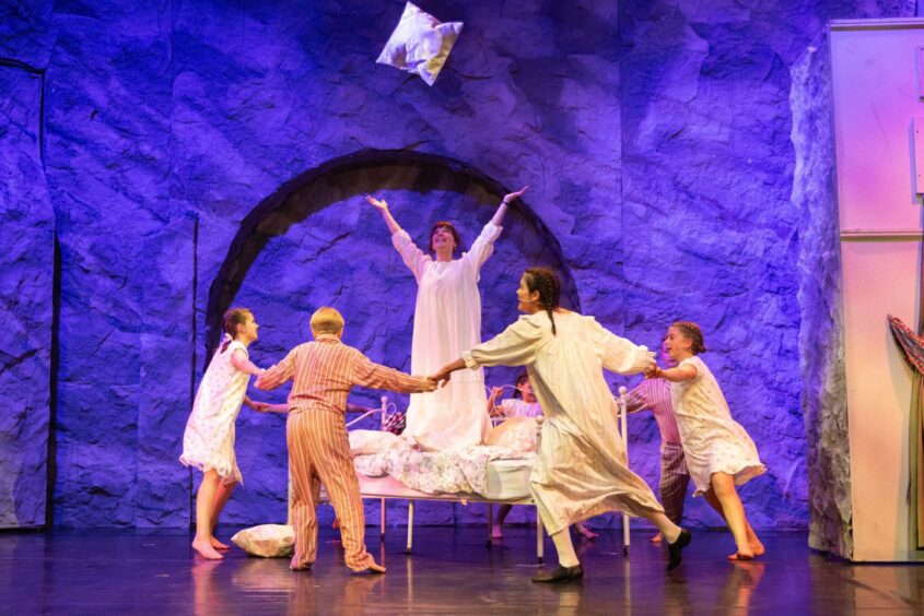 Maria stands on a bed throwing a cushion in the air as the Von Trapp children dance around her in an exuberant scene from The Sound of Music at Eden Court, Inverness.